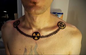 Фото тату на груди мужчины: черный символ радиации в окружении кельтских узлов, выполненных в графичном стиле.
