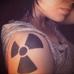 Фото простой татуировки с изображением символа радиации на плече, выполненной в черных тонах. Минималистичный и лаконичный рисунок.