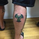 Фото минималистичной татуировки с зеленым символом радиации на икре. Простой и лаконичный рисунок татуировки.