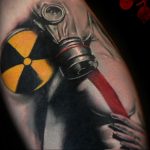 Фото тату: детализированный рисунок противогаза с желтым знаком радиации на фоне темного фона. Татуировка выполнена в реалистичном стиле с использованием теней и бликов.