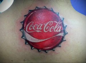 Фото татуировки на спине с изображением крышки от Coca-Cola. Рисунок выполнен в реалистичном стиле, с использованием ярких цветов и детализированной проработкой.