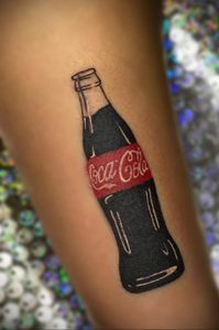 Фото тату бутылки Coca-Cola на руке. Черный контур, красная этикетка, реалистичный рисунок. Эскиз тату в стиле реализм.
