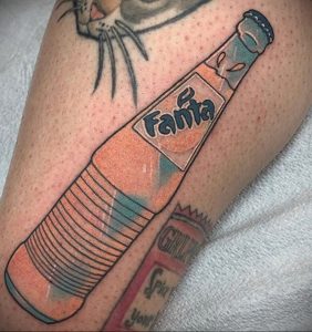 Фото тату бутылки Fanta на предплечье. Рисунок выполнен в ярких оранжевых и голубых тонах с черным контуром. Детализированный эскиз тату.