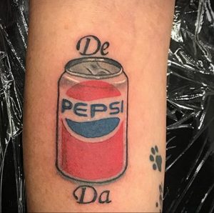 Фото тату: яркая татуировка банки Pepsi с надписью 'De Da' сверху и снизу. Цветная татуировка на руке.