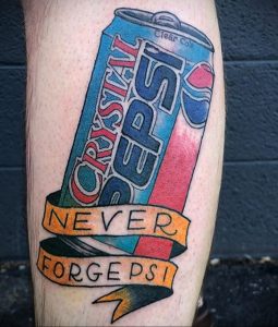 Цветное фото татуировки на ноге с изображением банки Crystal Pepsi и ленты с надписью 'Never Forget Pepsi'.