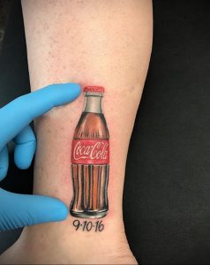 Фото тату на лодыжке с изображением миниатюрной бутылки 'Coca-Cola' и датой '9-10-16'. Символичный и запоминающийся рисунок.