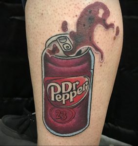 Фото тату на ноге с изображением открытой банки 'Dr Pepper', из которой выплескиваются брызги. Яркий и динамичный рисунок.