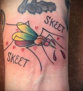 Фотография необычной татуировки мухи на руке с надписью "SKEET". Рисунок выполнен в ярких цветах с использованием традиционных элементов.