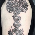 Фото тату на плече, изображающее дерево, корни которого переходят в спираль ДНК. Рисунок выполнен в черно-белой графике с высокой детализацией.