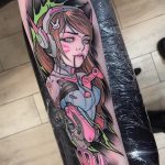 Фото татуировки на руке с изображением D.Va, персонажа из игры Overwatch, в окружении неоновых элементов и игрового контроллера.