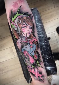Фото татуировки на руке с изображением D.Va, персонажа из игры Overwatch, в окружении неоновых элементов и игрового контроллера.
