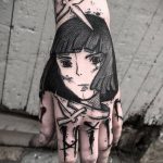Фото татуировки на руке с изображением девочки в стиле аниме. Черно-белый рисунок с минималистичными деталями и мрачной атмосферой.
