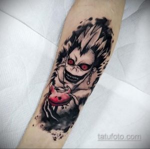 Фото татуировки на предплечье с изображением Лайта Ягами из аниме Death Note. Черно-белая графика, зловещее выражение лица и динамичная композиция.