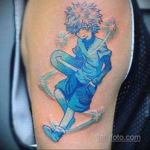 Цветное фото татуировки с изображением Гон Фрикса из аниме 'Hunter x Hunter' в динамичной позе на плече. Рисунок выполнен в ярких цветах с добавлением светящихся эффектов.