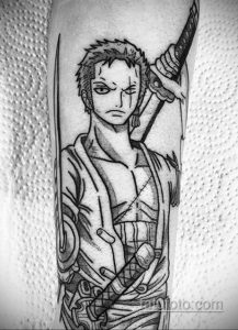 Фото тату на руке с изображением Зоро из One Piece, держащего меч. Черно-белый рисунок с высокой детализацией и динамичной позой.
