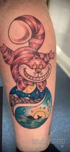 Фото яркой татуировки Чеширского кота, сидящего на глобусе. Оригинальный и красочный рисунок татуировки для поклонников Алисы в стране чудес.