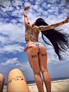 Фото тату с надписью "Kick Dick" на бедрах и татуировками на спине. Яркие цветы и узоры.