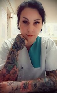 Фото тату на руке медсестры в белом халате. Рука украшена красочным рисунком с цветами, птицами и надписью.