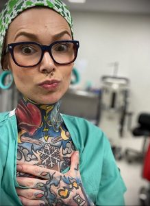 Фото тату на руках и шее у девушки-врача в зеленой медицинской форме и очках. Разноцветные татуировки в стиле олдскул и традишн.