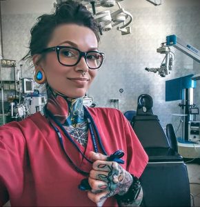Фото тату на руках и шее у девушки-врача в красном медицинском халате. Разноцветные татуировки в стиле олдскул и традишн.
