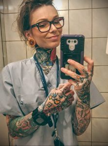 Фото тату на предплечье и шее у девушки-медсестры в медицинской форме. Разноцветные рисунки татуировок в стиле олдскул и традишн.