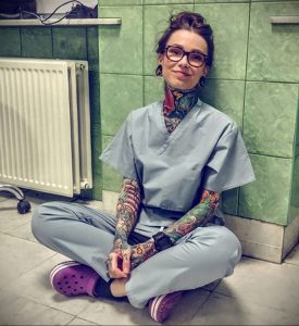 Фотография девушки-медика в медицинской форме с множеством татуировок на руках и шее. Яркие рисунки, демонстрирующие индивидуальность.