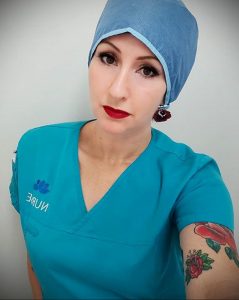 Фотография медсестры в бирюзовой униформе и голубой шапочке с татуировкой розы на руке. Женщина смотрит в камеру, на лице яркий макияж.