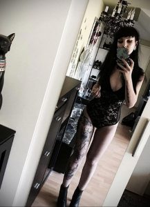 Фото тату на ноге девушки в черном боди. Рисунок татуировки включает в себя темные узоры и детали.