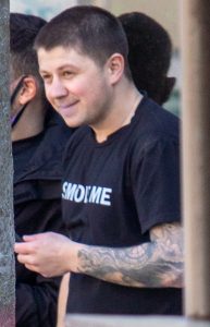Фото мужчины с татуировкой на руке, изображающей волны. Мужчина улыбается и выглядит расслабленным.