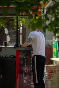 Фото тату на руке мастера, работающего на улице. Черно-серый рисунок с элементами готики и символизма, вид сзади.