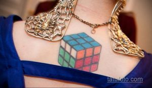Фото миниатюрной татуировки кубика Рубика на ключице. Татуировка выполнена в ярких цветах, с четкой прорисовкой граней.