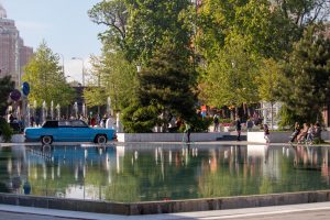 Фотография городского парка с фонтаном и голубым автомобилем. Акварельный стиль, яркие цвета, отражения в воде, вдохновение для тату.