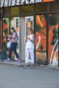 Фотография девушки в белом костюме с татуировками тигра на руках, стоящей на улице возле магазина.