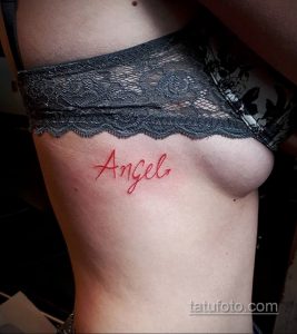 Фото татуировки надписи "Angel" на боку. Надпись выполнена красным цветом, шрифт рукописный и изящный. Нежная и женственная татуировка.