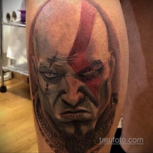 Фото тату с изображением Кратоса, персонажа из игры God of War, на плече. Реалистичный портрет с красным символом на лбу.