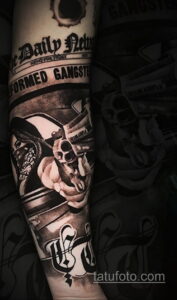 Фото тату: черно-белая татуировка в гангстерском стиле на руке. Изображение человека в шляпе и с пистолетом, газетный фон, надписи.