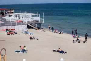 Фотография пляжа с отдыхающими людьми и видом на море. На переднем плане видны лежаки и люди, загорающие на песке.