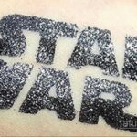 Фотография глиттер-татуировки с надписью "STAR WARS", выполненной черными блестками на коже. Идеально для поклонников саги.
