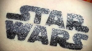 Фотография глиттер-татуировки с надписью "STAR WARS", выполненной черными блестками на коже. Идеально для поклонников саги.