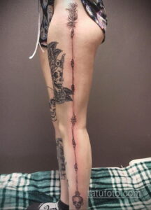 Фото тату черепа, пронзенного стрелой на бедре. Черно-белая татуировка в стиле графика. Детализированный рисунок татуировки.