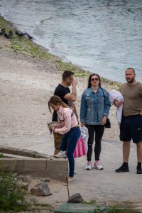 Фотография людей на берегу моря, у одного из них видна татуировка на плече. Снимок сделан в солнечный день, передает атмосферу отдыха.