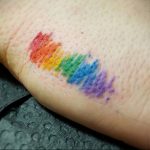 Фото миниатюрной татуировки радуги на пальце. Яркие цвета, акварельный эффект, минималистичный дизайн. Идеи для тату, эскизы татуировок.