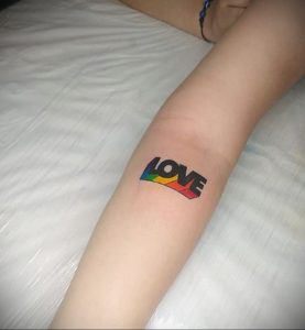 Фото татуировки с надписью 'Love' на руке, выполненной в радужных цветах. Яркие цвета, минималистичный дизайн.