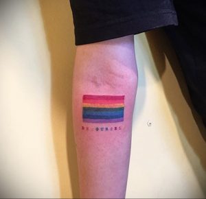 Фото минималистичной татуировки на руке с изображением радуги и надписью 'Be yourself'. Мотивирующая фраза, яркие цвета.