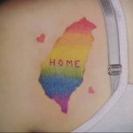 Фото тату: контур карты Тайваня, залитый цветами радуги, с небольшими сердечками и надписью 'HOME', выполненное на плече.
