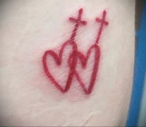 Фото татуировки с изображением двух красных сердец, пронзенных двумя крестами. Символичный и эмоциональный рисунок.