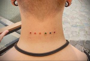 Фото татуировки с изображением нескольких маленьких радужных точек, расположенных на затылке. Минималистичный и необычный рисунок.
