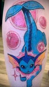 Яркая татуировка с изображением покемона Vaporeon в стиле аниме, выполненная в голубых и розовых тонах на ноге.
