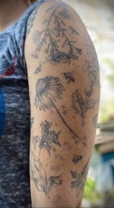 Фото татуировки в стиле ботанический рукав. Ромашки, пчелы, листья, черно-белый рисунок.