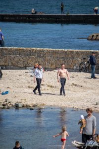 Фото тату на руке мужчины: черно-серый рисунок, частично видимый на плече, на фоне морского пейзажа. Идеально для демонстрации тату на открытом воздухе.